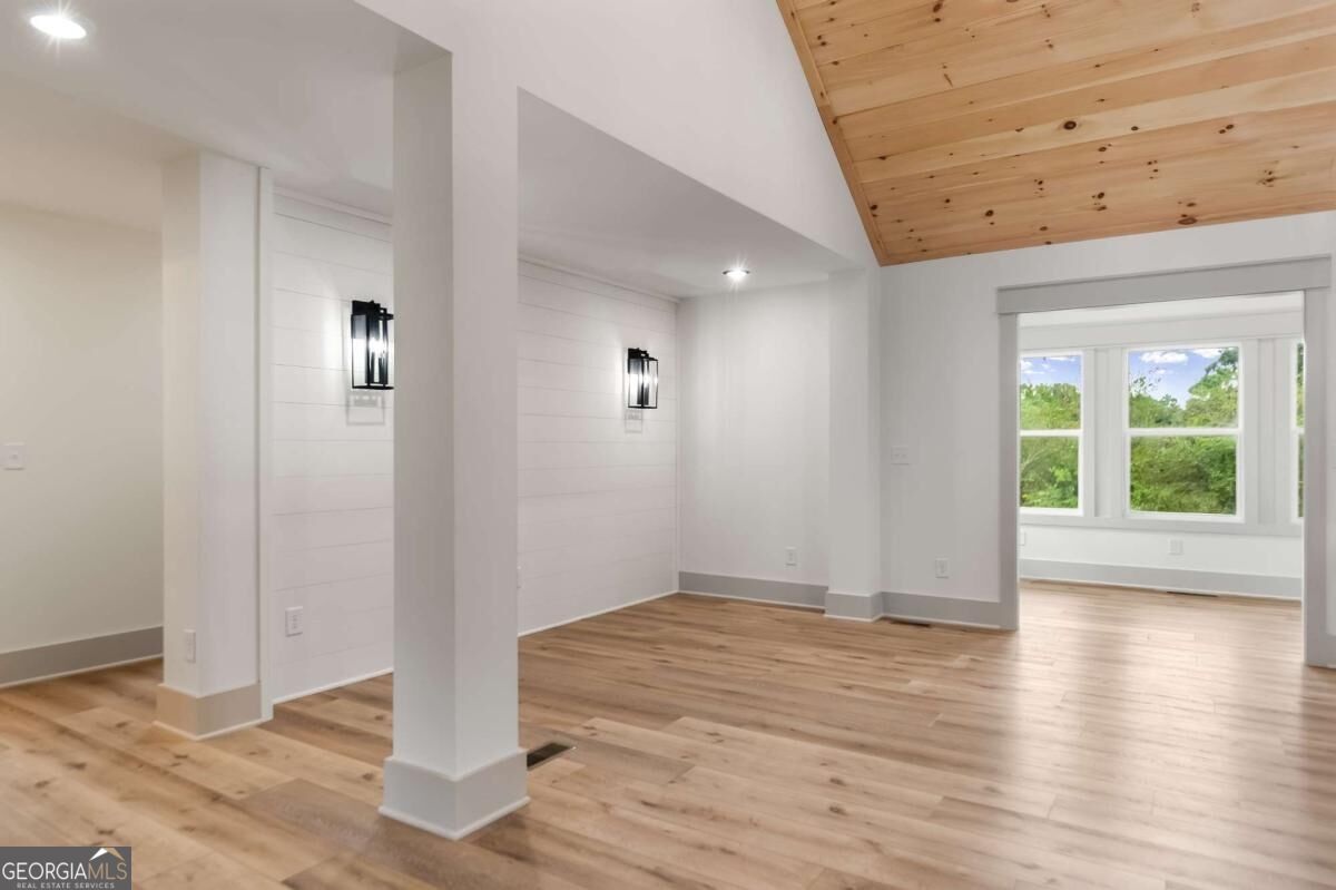 Empty room with wood plank floors, a wood-plank ceiling section, and windows overlooking greenery.