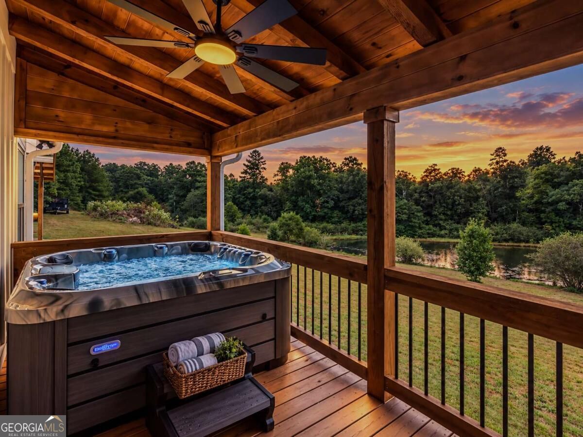 Covered deck hot tub overlooking a pond and trees at sunset.