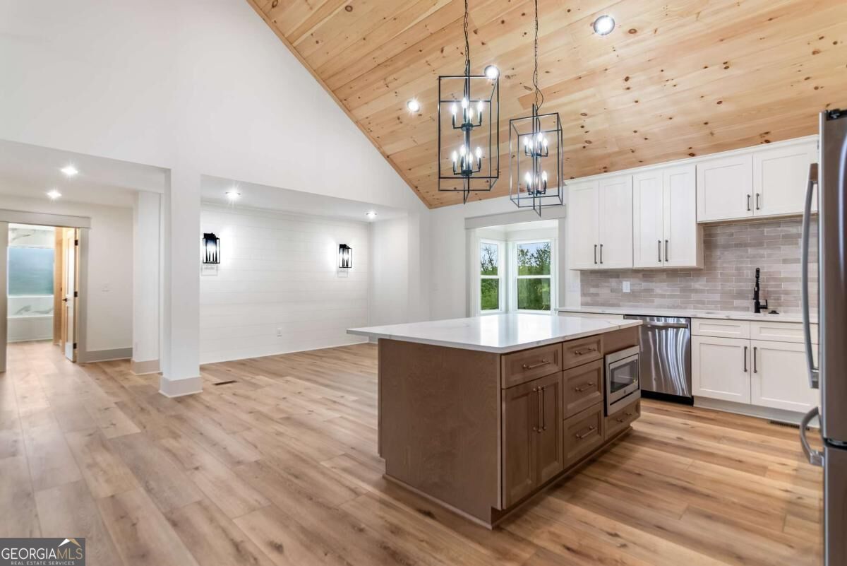 Open kitchen with a large wood island, white cabinets, and a vaulted wood ceiling.