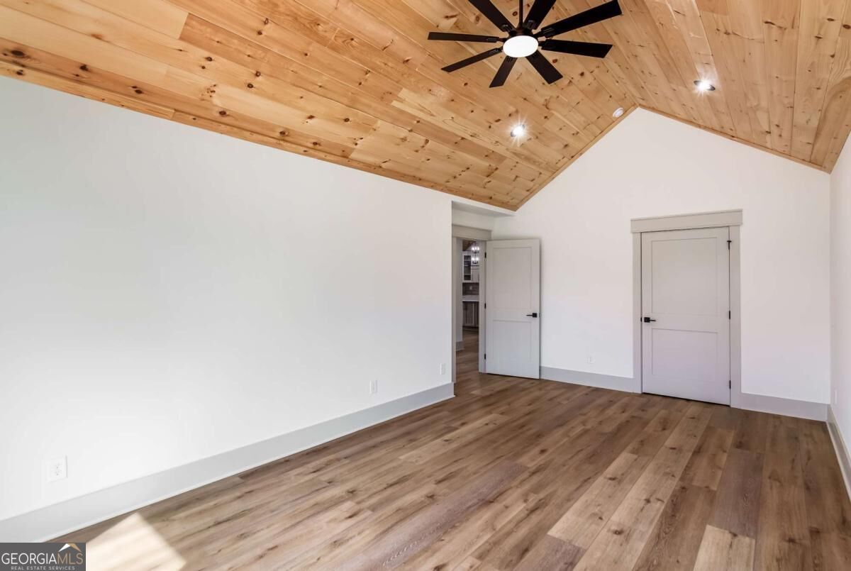 Empty room with a vaulted wood ceiling, black ceiling fan, and wood flooring.