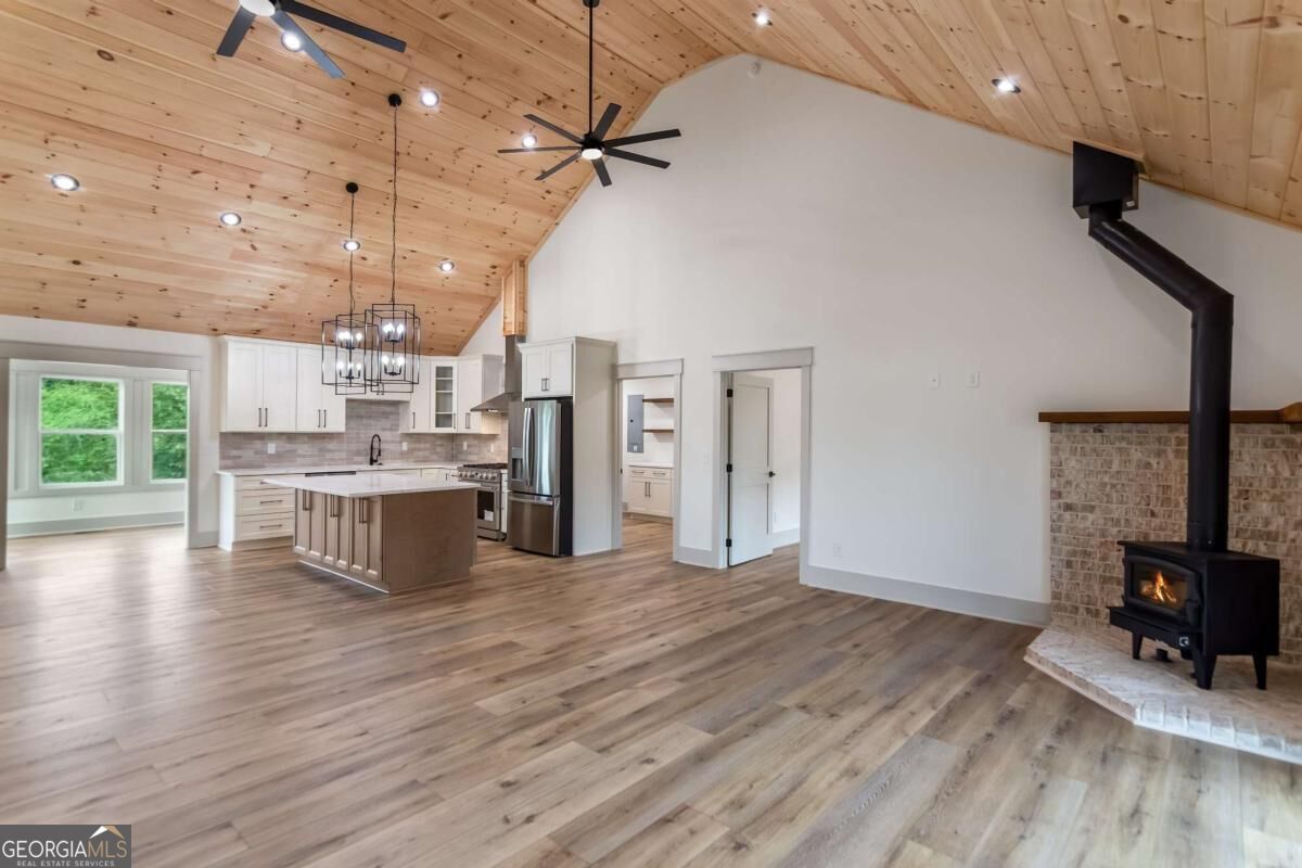 Open-plan kitchen and living area with a vaulted wood ceiling, large island, and black wood stove.