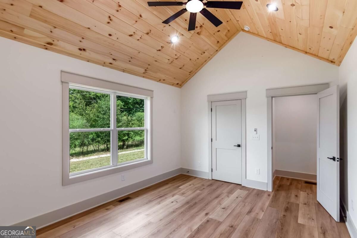 Empty room with a vaulted wood ceiling, black ceiling fan, large window, and wood-look floors.