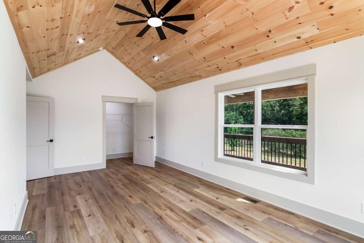 Empty bedroom with a vaulted wood-plank ceiling, ceiling fan, closet, and window overlooking trees.