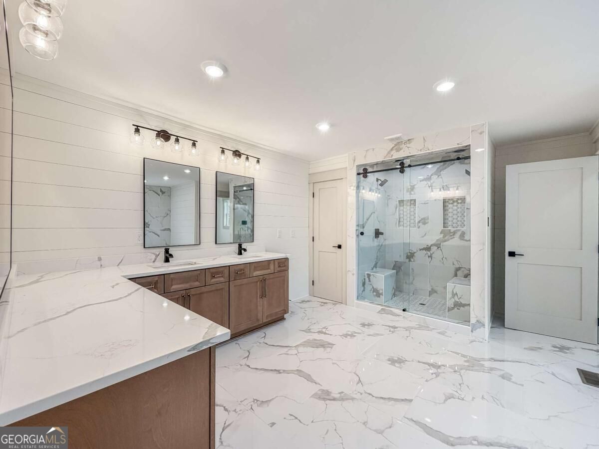 Bathroom with a double vanity, marble-look surfaces, and a glass-enclosed shower.