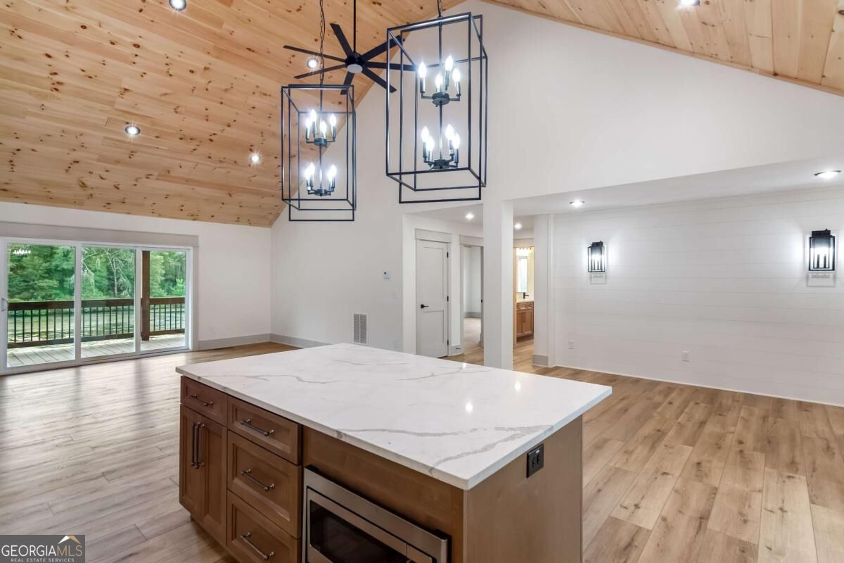 Open-plan kitchen with a large stone-topped island, vaulted wood ceiling, and sliding doors to a wooded deck.