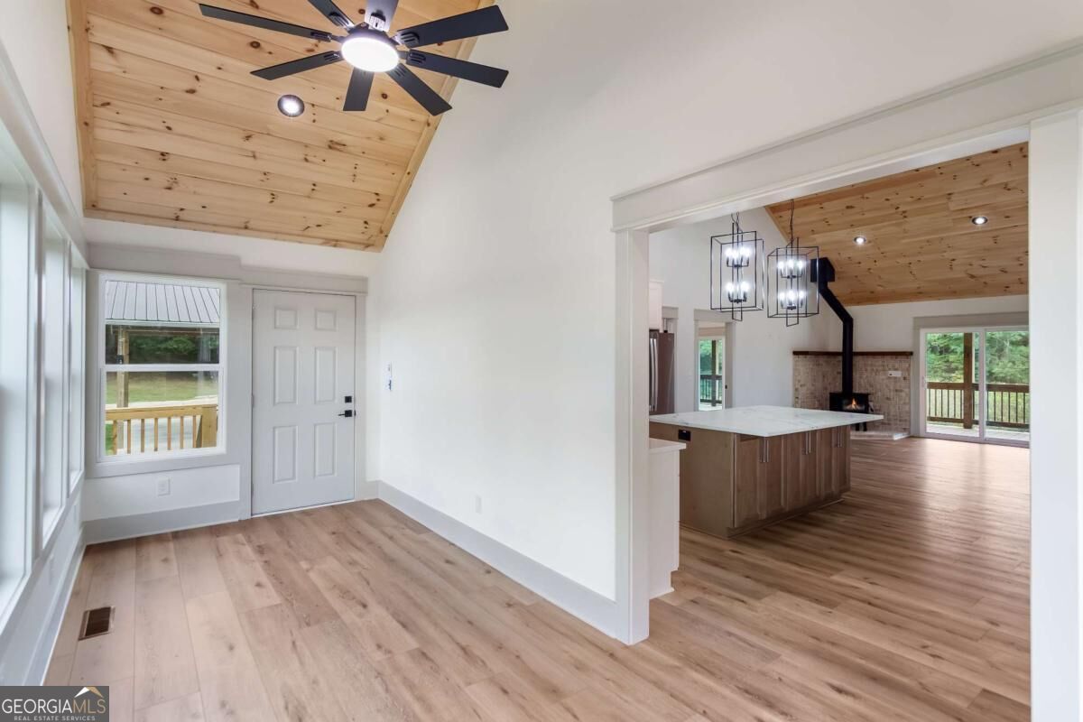 Entry area with light wood floors and pine ceiling opens to a kitchen with an island and fireplace.