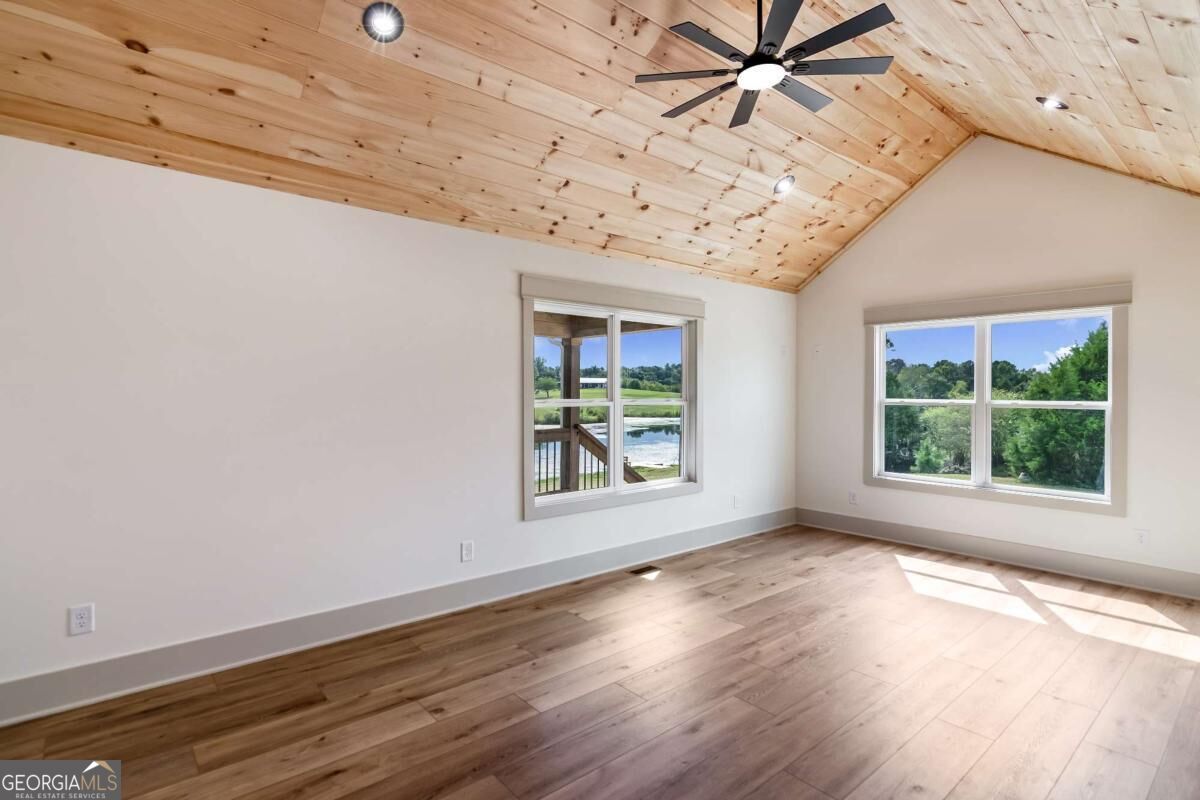 Empty room with a vaulted wood ceiling, ceiling fan, and windows overlooking greenery and water.