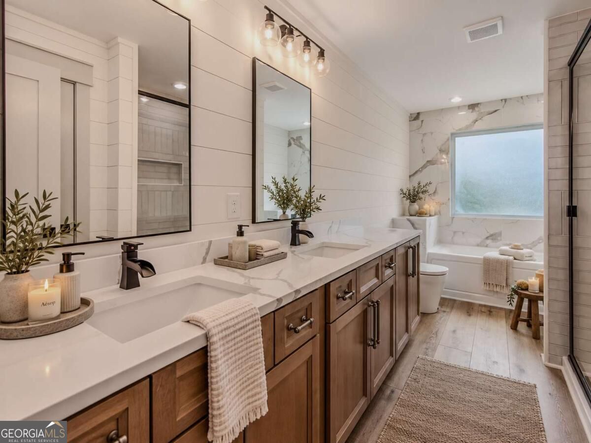 Bathroom with a double wood vanity, marble-look surfaces, and a tub beneath a large window.