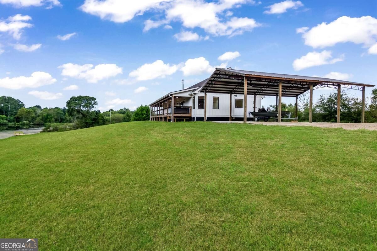 Home with a large open-sided metal boat shelter on a grassy lot beside the water.