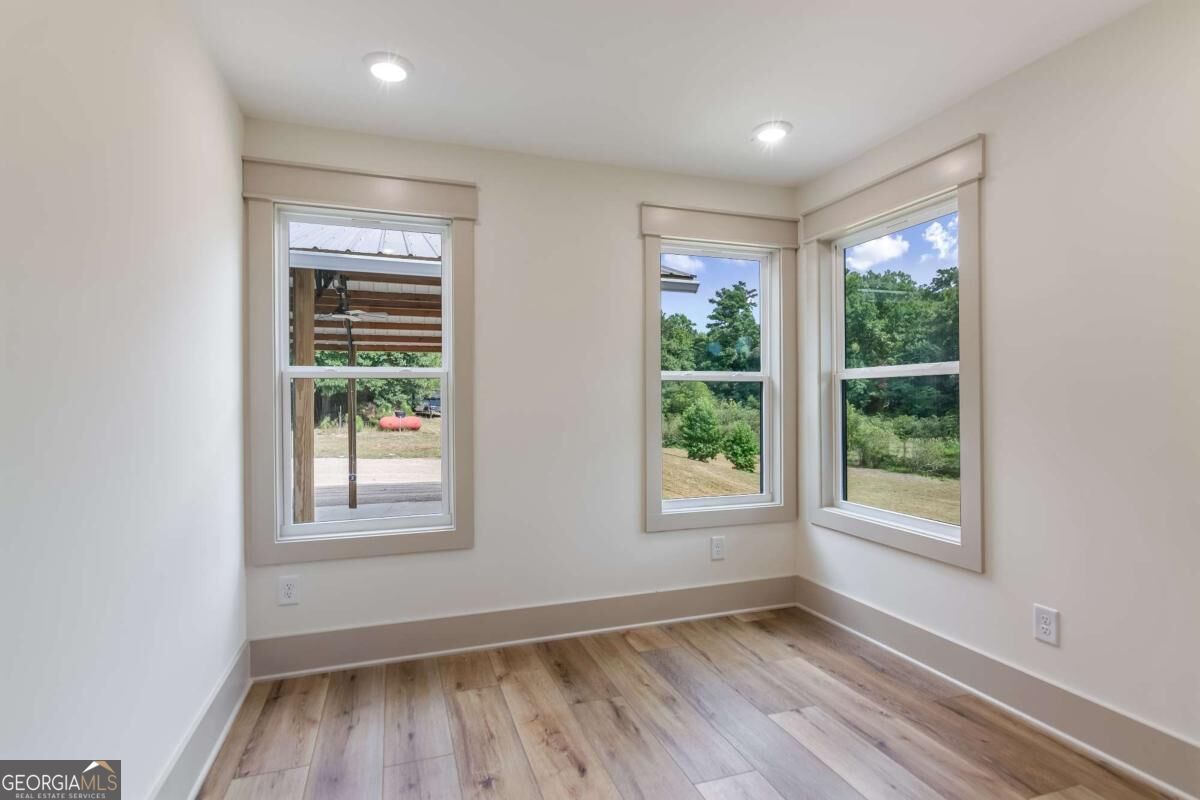 Empty room with wood-look flooring and three windows overlooking a green yard.