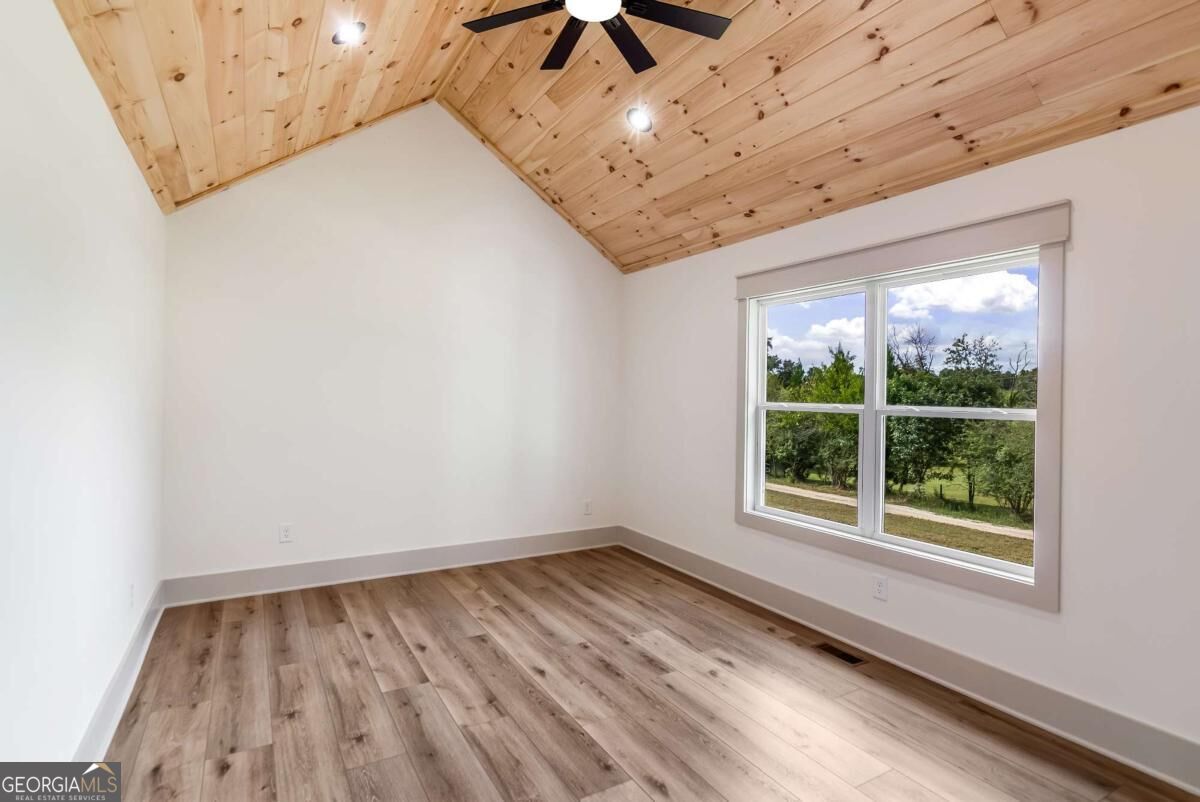 Empty room with a vaulted pine ceiling, wood-look floors, and a large window overlooking trees.
