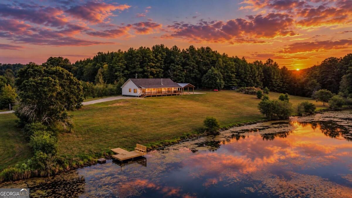 Aerial view of a home beside a pond, with a wooden dock and sunset reflections.