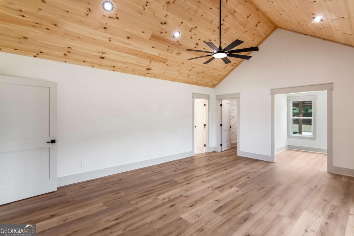 Empty room with a vaulted pine ceiling, ceiling fan, and light wood floors.