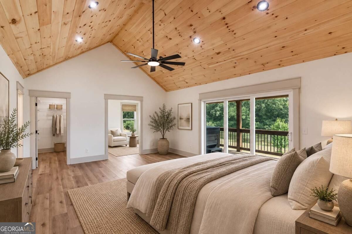 Bedroom with a vaulted wood-plank ceiling, large bed, and sliding doors to a tree-lined deck.