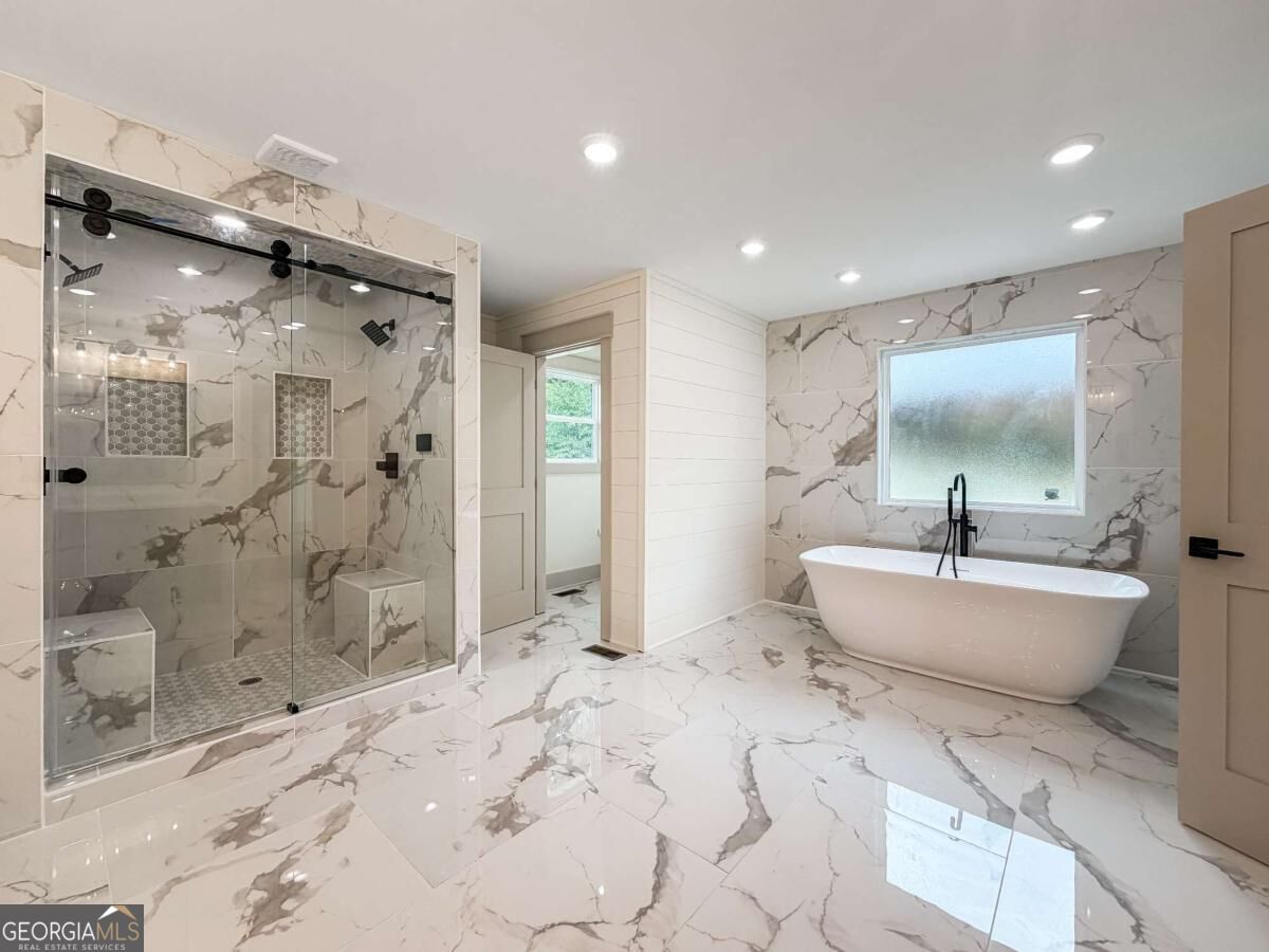 Bathroom with a glass-enclosed shower and freestanding tub, finished in marble-look tile.