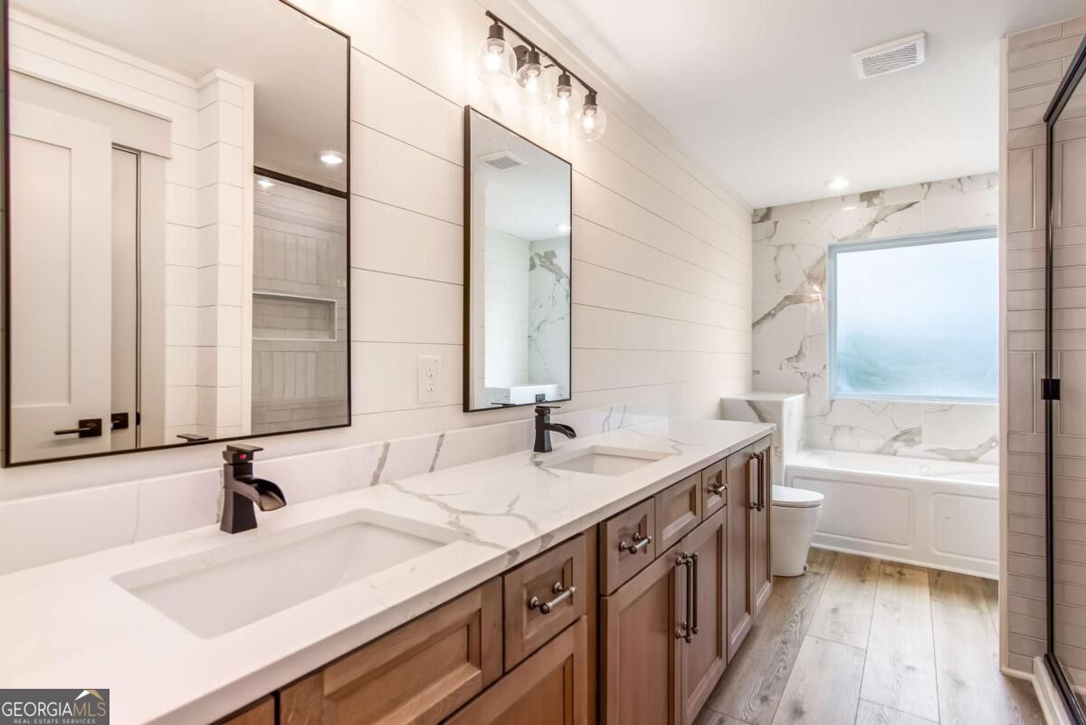 Bathroom with a double-sink wood vanity and marble-look bathtub surround beneath a frosted window.