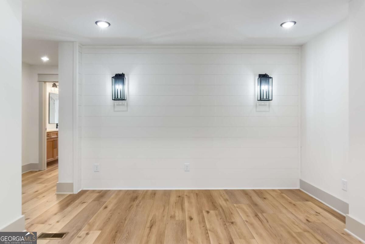 Empty room with wood flooring, a white shiplap wall, and two black wall sconces.