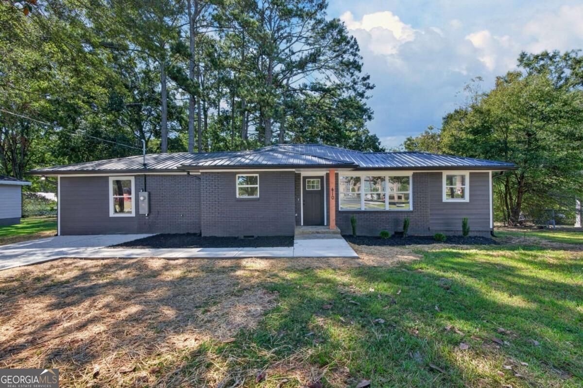 Single-story gray home with a metal roof, white-trimmed windows, and mature trees in the yard.