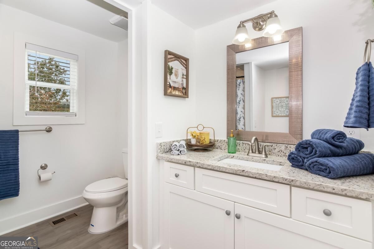 Bathroom with a white vanity, speckled countertop, large mirror, and separate toilet nook.