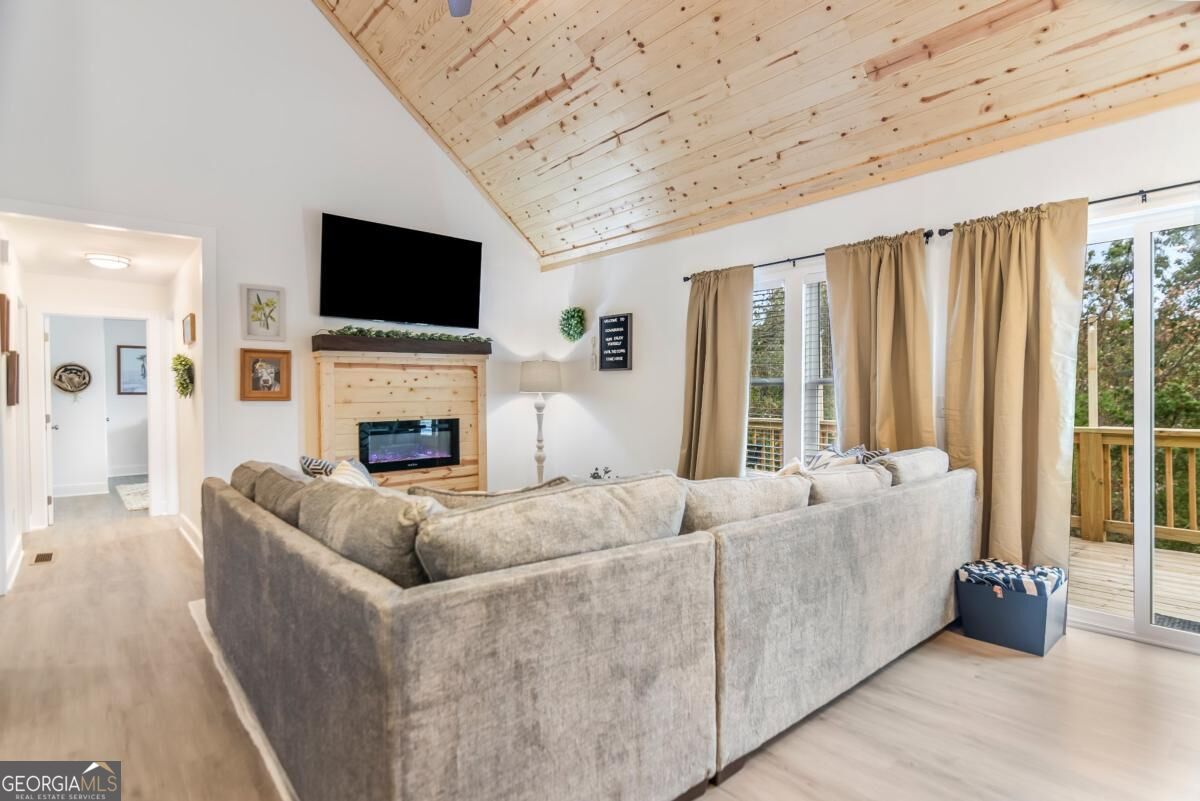 Living room with a vaulted wood ceiling, fireplace, large sectional, and sliding doors to a deck.