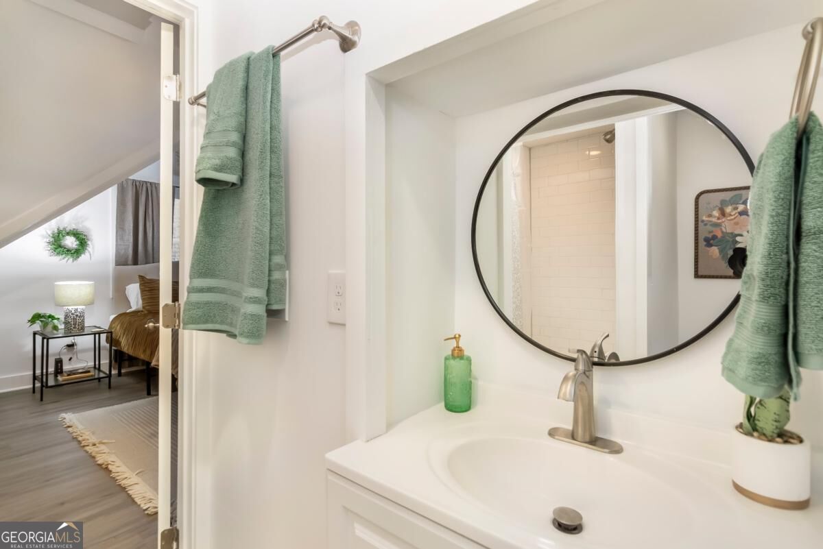 Bathroom vanity with a round mirror and green towels, opening onto a bedroom.