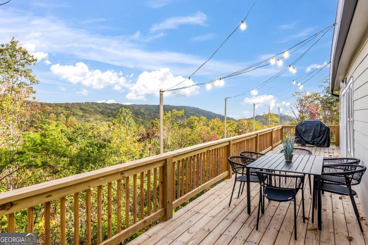 Wooden deck with outdoor dining set and string lights overlooking autumn-colored wooded hills.