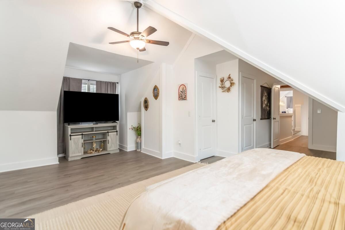 Attic bedroom with a sloped ceiling, bed, ceiling fan, and television.
