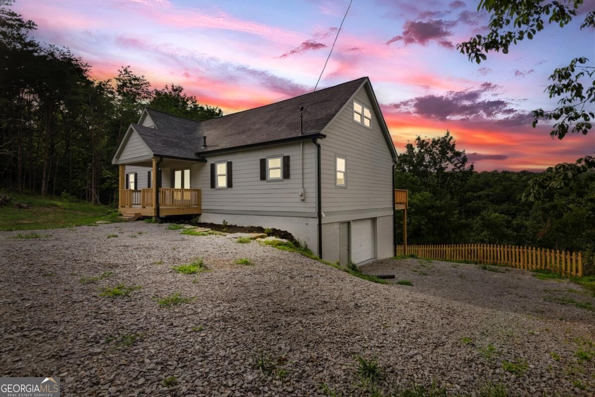 Gray-sided home with a gravel driveway and wooden porch beneath a vivid pink dusk sky.