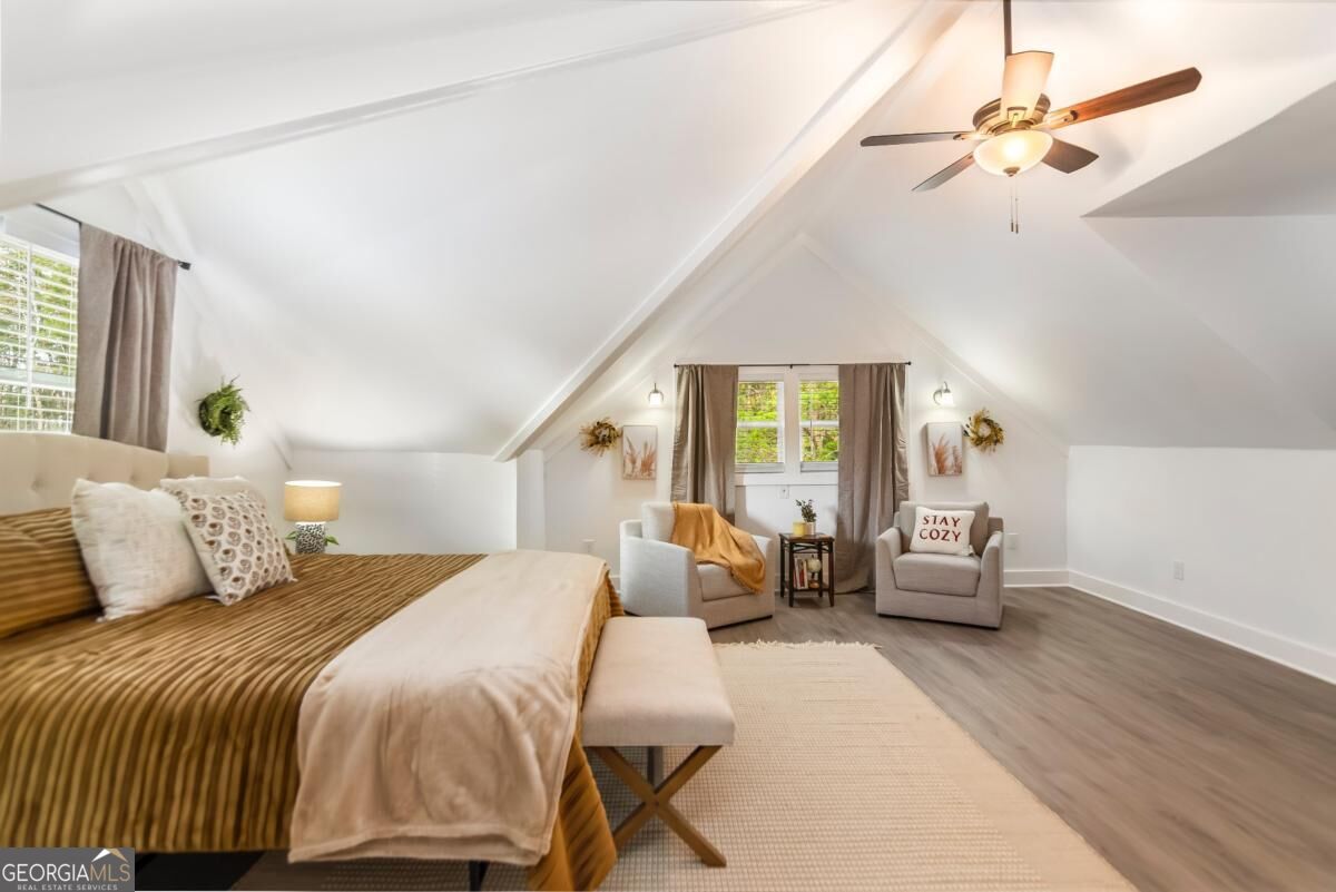 Staged attic bedroom with vaulted ceiling, striped bedspread, and cozy sitting area.