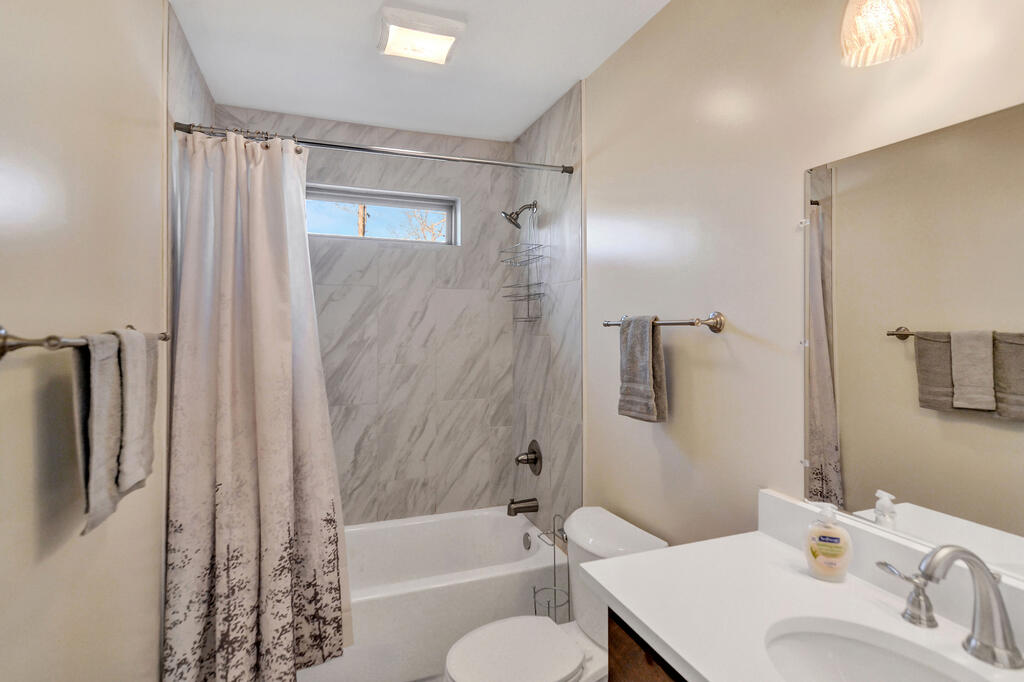 Bathroom with a marble-look tub surround, patterned shower curtain, and white vanity.