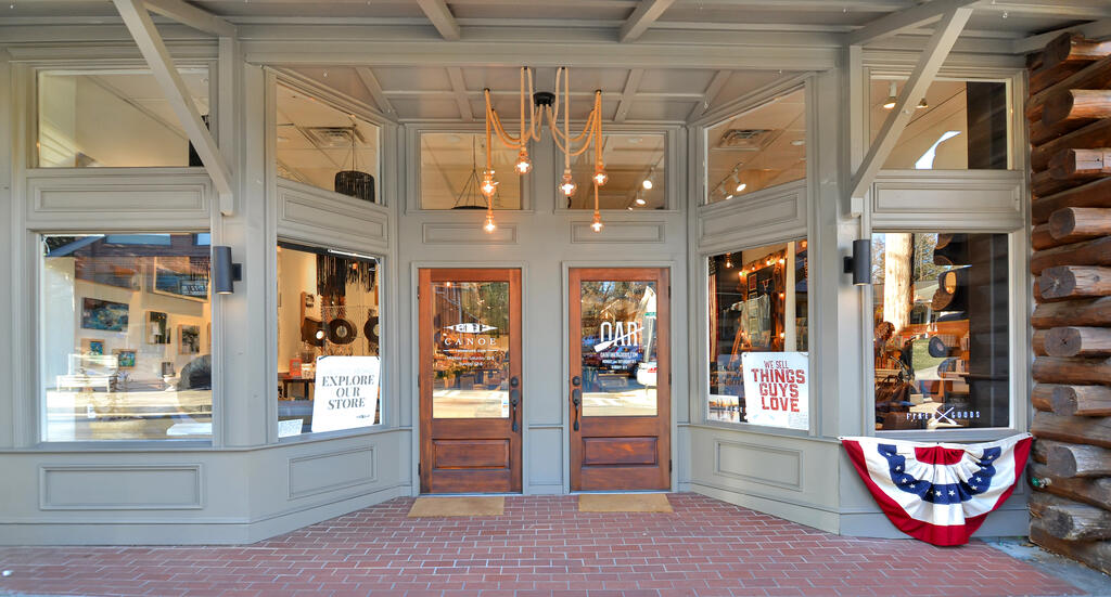 Gray storefront with wood-framed double doors, display windows, and patriotic bunting.