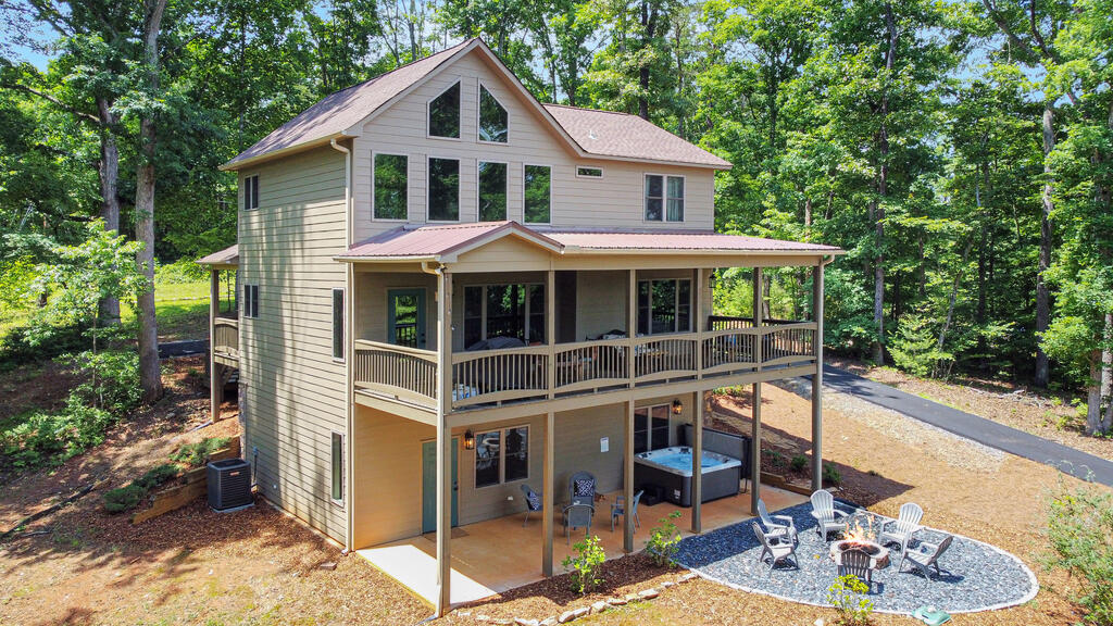 Two-story home with a spacious covered porch, hot tub, and fire-pit patio among trees.