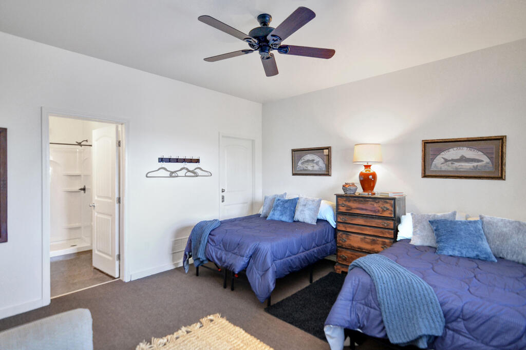 Bedroom with two blue-purple beds, a wooden chest of drawers, and an open bathroom doorway.