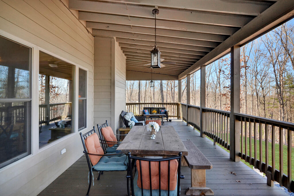 Covered deck with a long dining table and cushioned chairs overlooking leafless woods.
