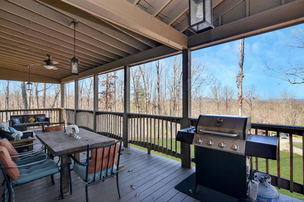 Covered deck with outdoor seating and a gas grill overlooking leafless woods and rolling hills.