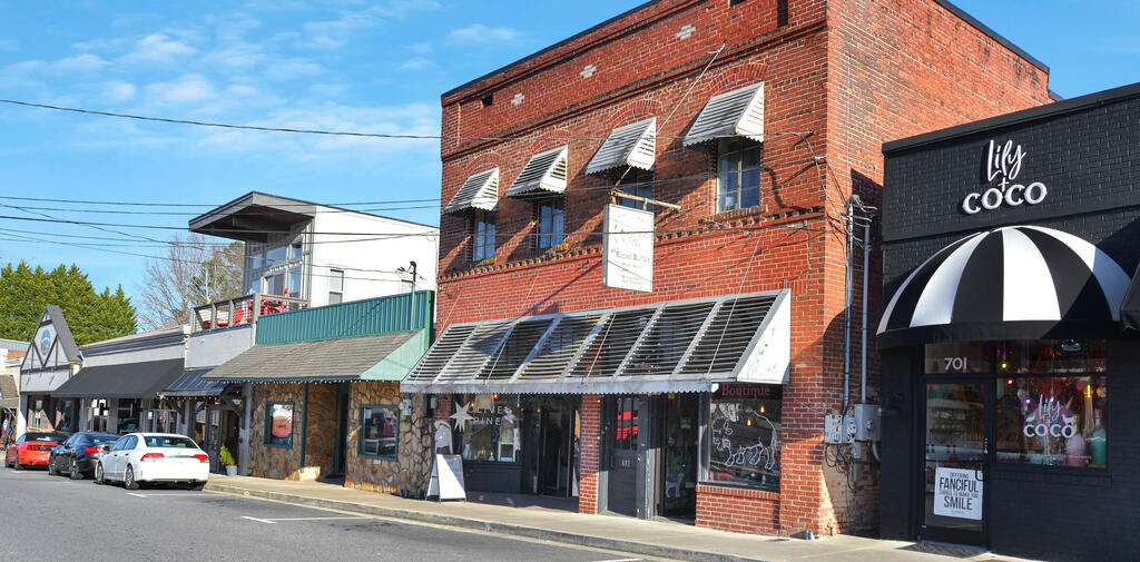 Commercial storefronts on a sunny street, with a red-brick building and a black-and-white striped awning.