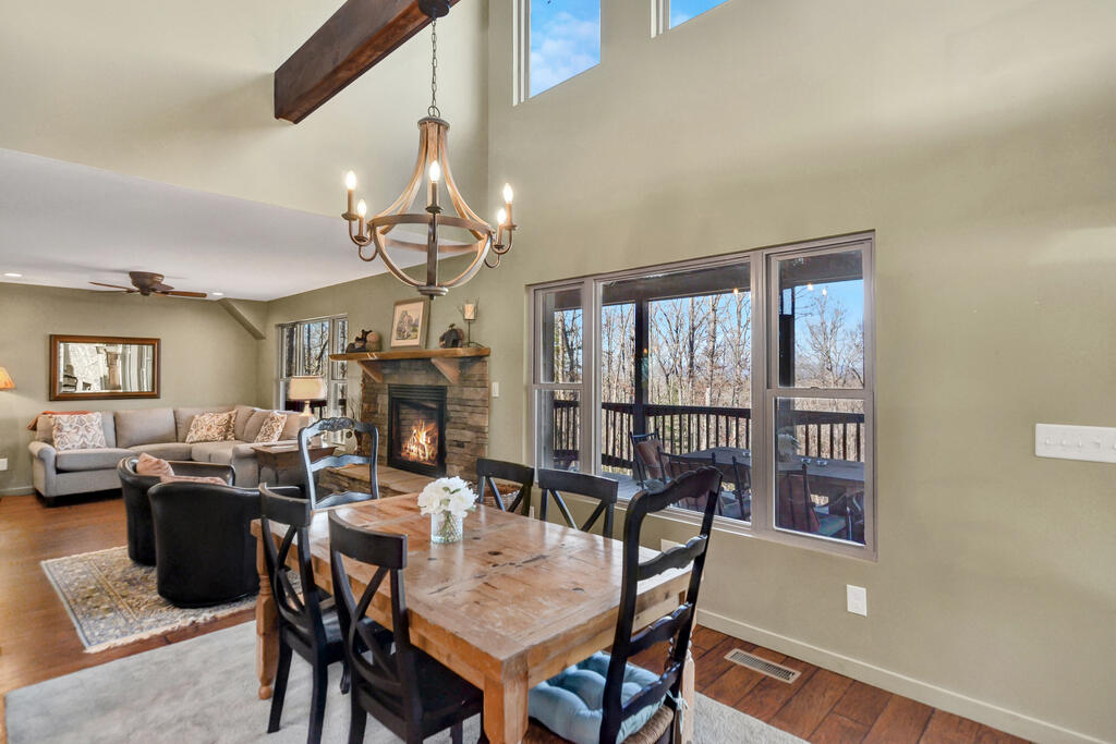 Open-plan dining and living area with a stone fireplace and windows overlooking leafless trees.