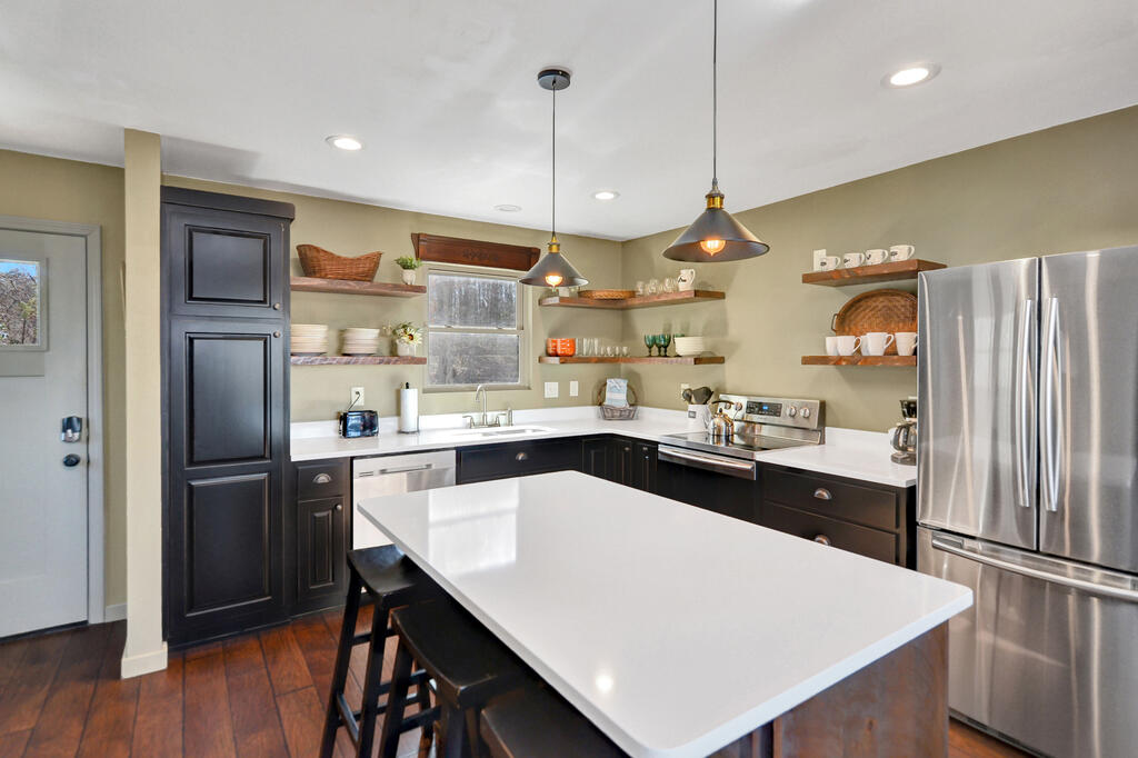 Kitchen with a large white island, dark cabinets, stainless steel appliances, and open dish shelves.