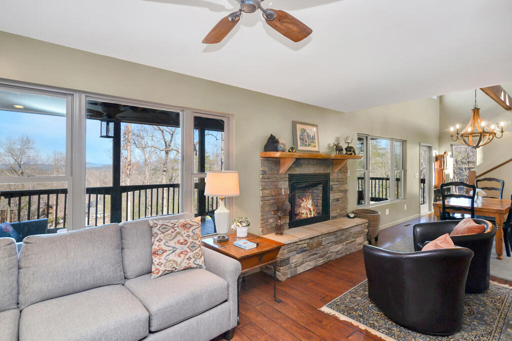 Living room with a stone fireplace, large deck-facing windows, and distant mountain views.