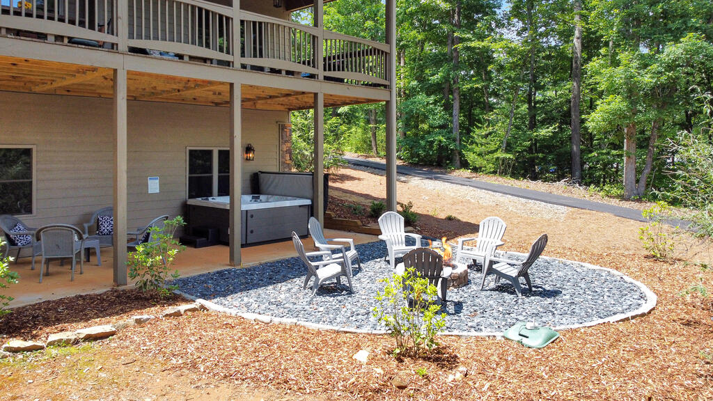 Outdoor patio with a hot tub beneath a raised deck and a fire pit seating area beside the woods.