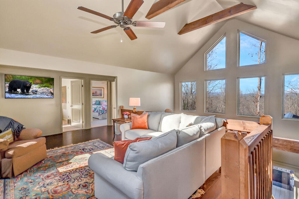 Vaulted living room with exposed beams, large windows, and a wooded view.