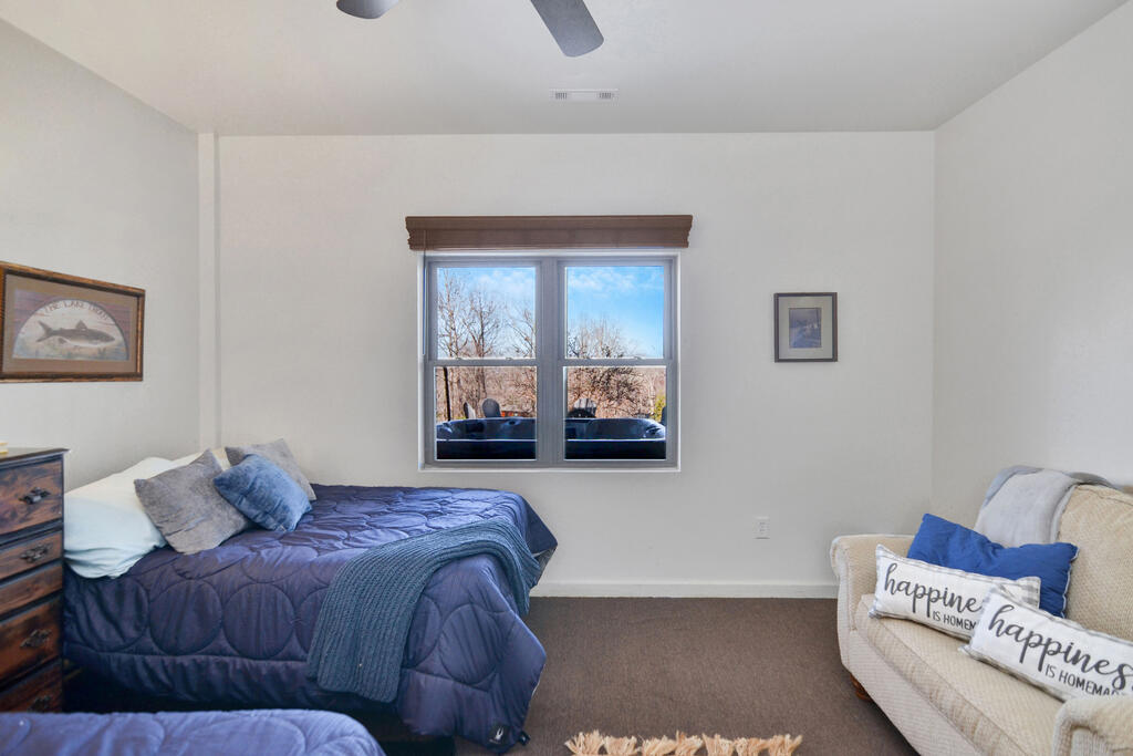 Bedroom with a blue quilted bed, cream loveseat, and window overlooking leafless trees.