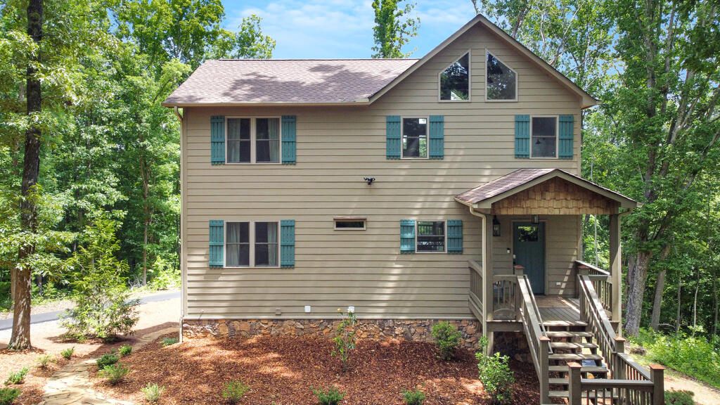Two-story beige house with teal shutters and a covered front porch, surrounded by trees.