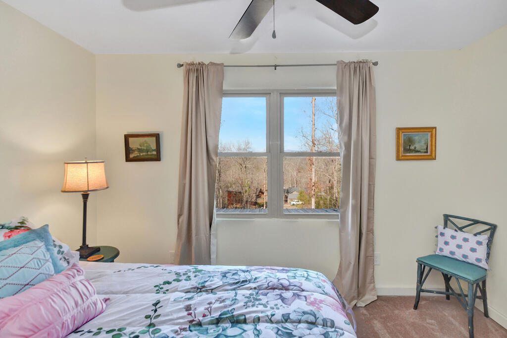 Bedroom with a floral bedspread and a large window overlooking trees and distant hills.