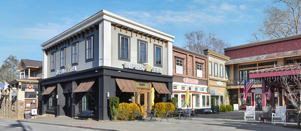 Row of downtown storefronts with a dark corner building, striped awnings, and outdoor café seating.