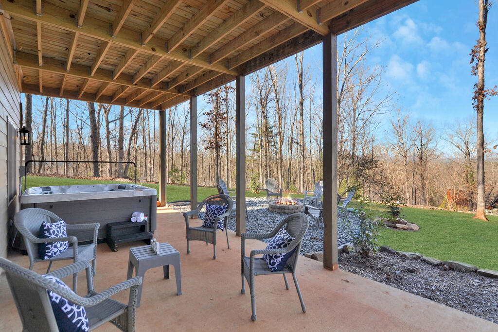 Covered patio with wicker seating and hot tub overlooking a lawn and leafless woodland.