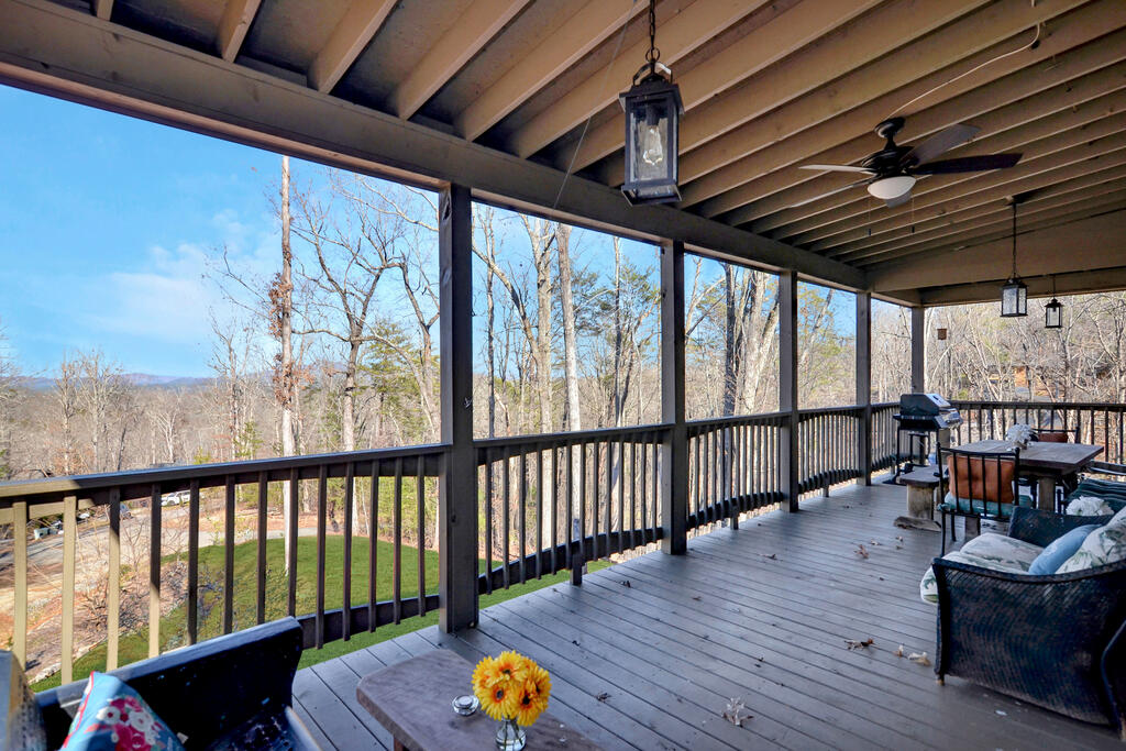 Covered deck with outdoor seating overlooking a lawn, leafless woods, and distant mountain ridges.