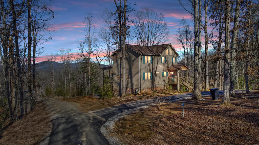 Two-story wooded home with a curved driveway and distant mountain view at dusk.