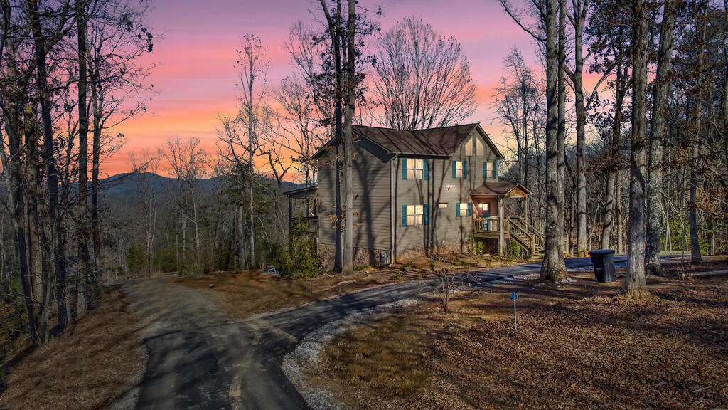 Two-story house among leafless trees, with a curved driveway and mountain ridge at dusk.