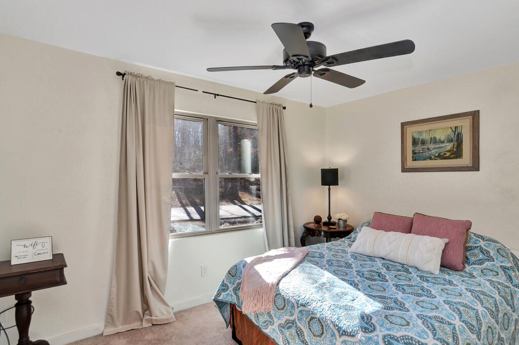 Bedroom with a blue patterned quilt, beige curtains, and a dark ceiling fan.